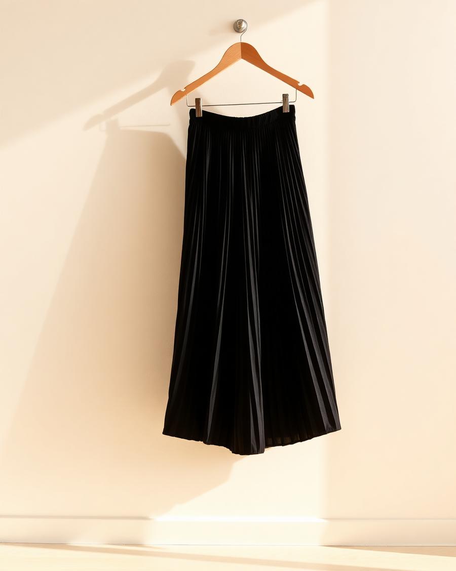 A black pleated skirt hanging against an ivory wall